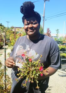 Alameda Post -Ploughshares manager Jordan Taylor smiling and holding a plant