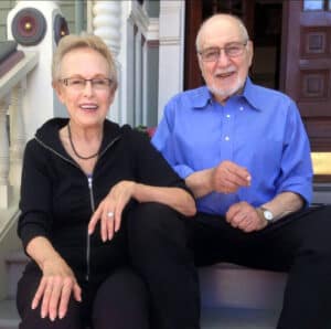 Alameda Post - a couple sits on the steps of their home and smiles. Arthur and Gretchen Lipow.