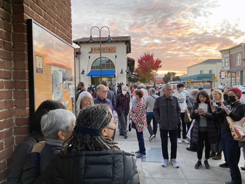 Alameda Post - a crowd gathers and takes photos of a new historical marker for Tonarigumi on a brick building 