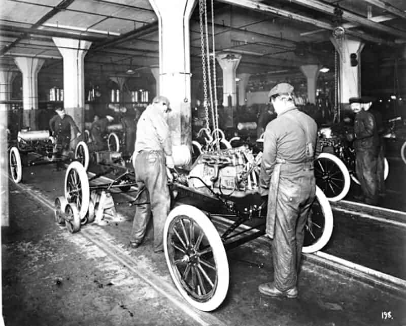 Alameda Post - a black and white photo of two men assembling a Model T on a moving assembly line