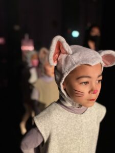 Alameda Post - a young performer in a mouse costume and facepaint is illuminated by bright stage lights