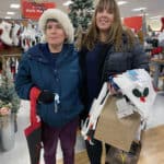 Alameda Post - two women pose together in a department store together holding armfuls of items and smiling