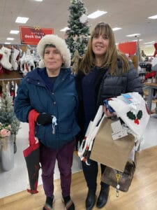 Alameda Post - two women pose together in a department store together holding armfuls of items and smiling