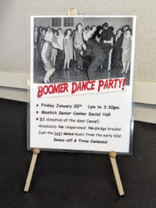 Alameda Post - a sign is set up at the event with a large black and white photo of people dancing. It says "Boomer Dance Party! Friday January 20th. 1pm to 3:30 pm. Mastick Senior Center Social Hall. $2 donation at the door (wow!) Absolutely no chaperones! No pledge breaks! Just the best dance music from the early 60s! Dane-off & Trivia Contests!"