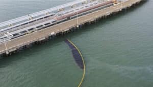 Alameda Post - a large black splotch of oil in the ocean is partially contained by a yellow barrier
