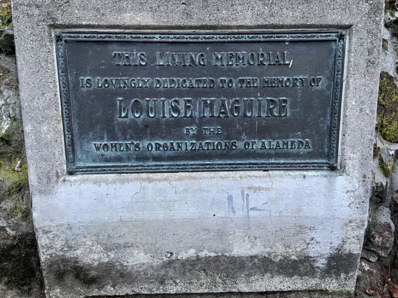 Alameda Post - a plaque on a large rock at The Rockery reads "This living memorial is lovingly dedicated to the memory of Louise Maquire by the Women's Organizations of Alameda." There is blank space on the rock below the plaque