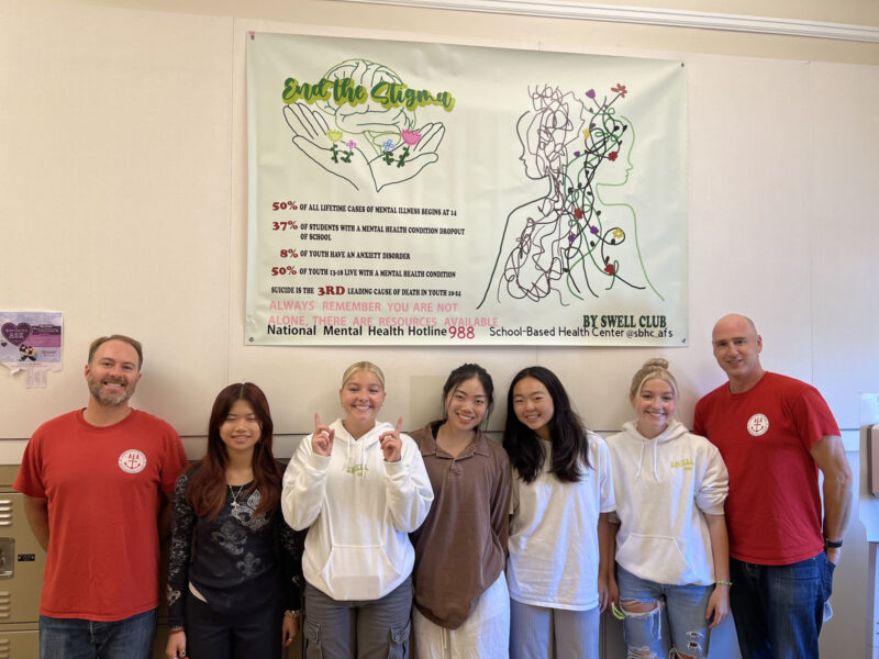 Alameda Post- faculty and students stand in front of a poster on the wall. It says "End the Stigma. " and includes statistics about mental health. National Mental Health Hotline 988