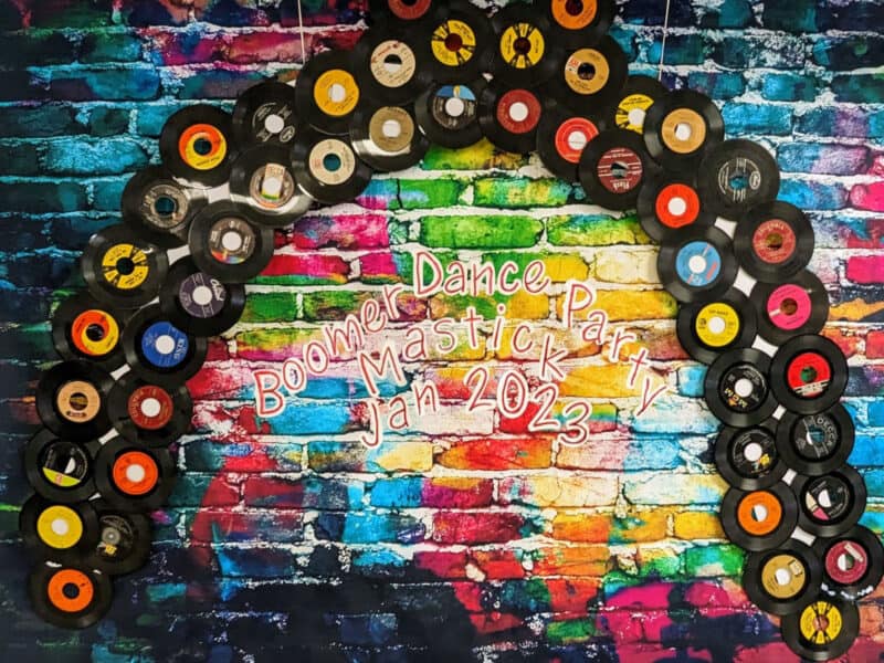 Alameda Post - the selfie station for taking photos is a brick wall covered in a rainbow of paint. Records hang from the ceiling in the shape of a rainbow arch. In the middle, the words "Boomer Dance Party Mastick Jan 2023"