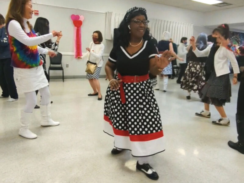 Alameda Post - a woman in a polka dot black, white, and red dress dances amongst the attendees at the Boomer Dance Party