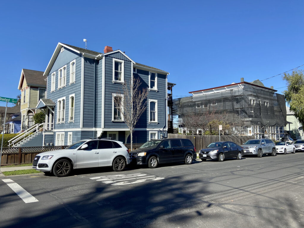 Alameda Post - a large blue house on a street corner with cars parked along the road