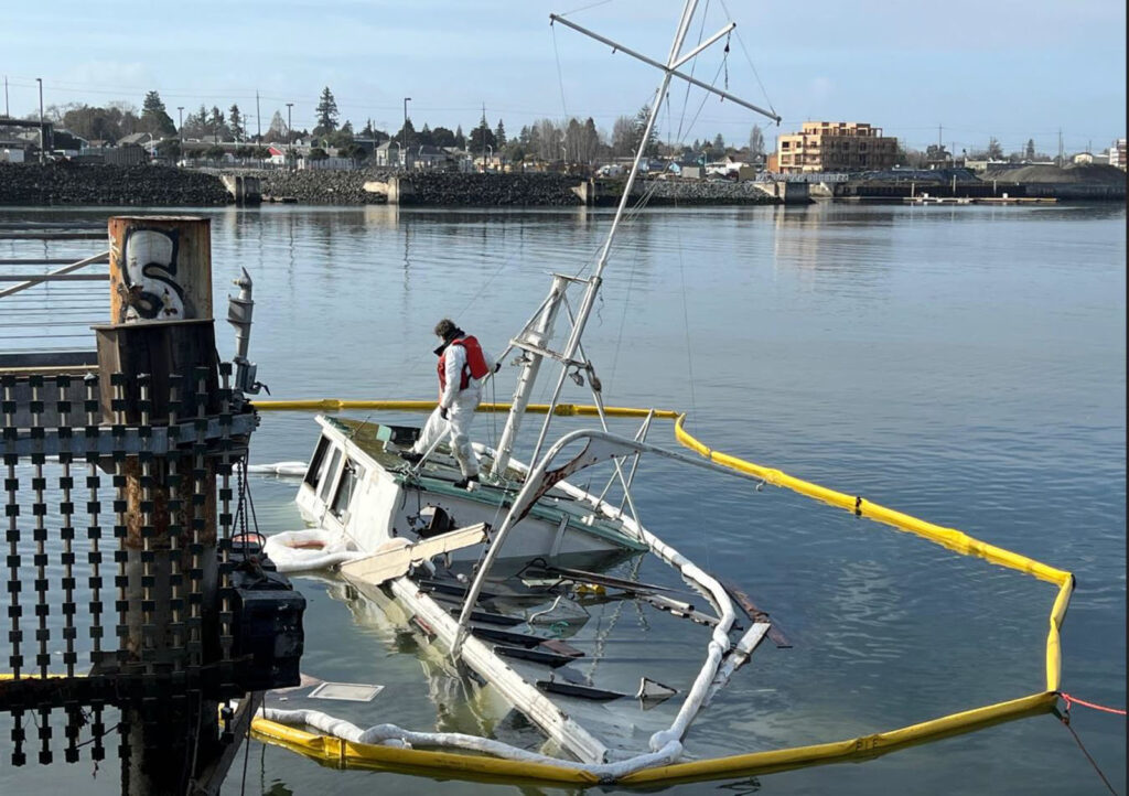 Alameda Post - a man stands on top of a sunk boat. It is encircled in a bright yellow floating circle