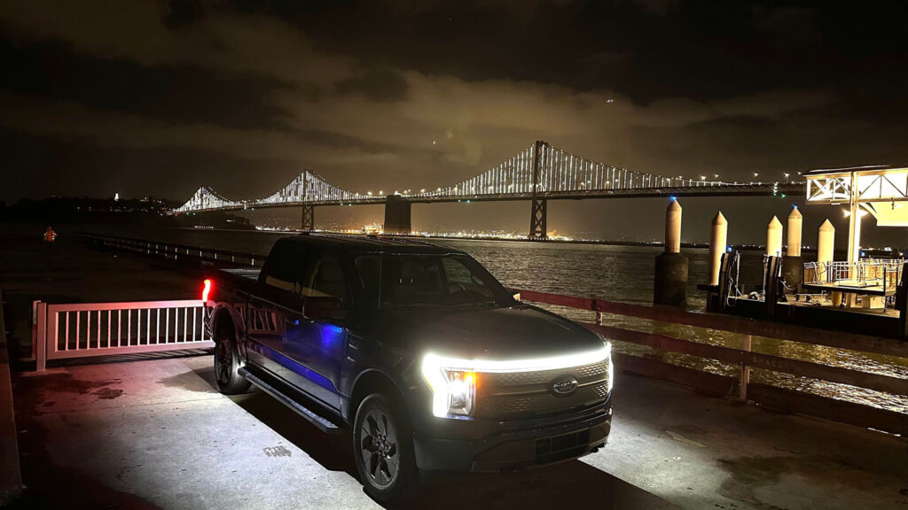 Alameda Post - a nighttime photo of a truck with the background of the lit up Bay Bridge