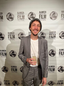 Alameda Post - Leland Montgomery stands in front of a background that says Alameda Film Festival and smiles