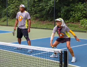 Alameda Post - two pickleball players. One swings at the ball on the court