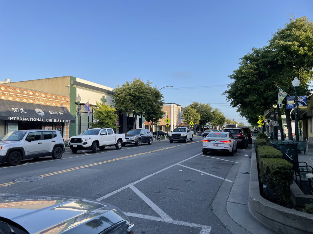 Alameda Post - a section of roadway with some cars parked, painted lines, and some cars parked over the painted lines