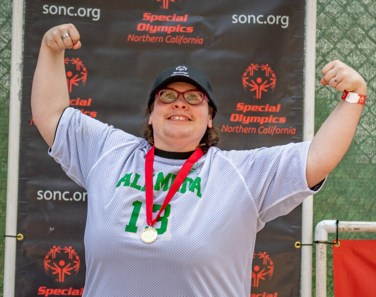 Alameda Post - an athlete with a medal around their neck flexes and smiles
