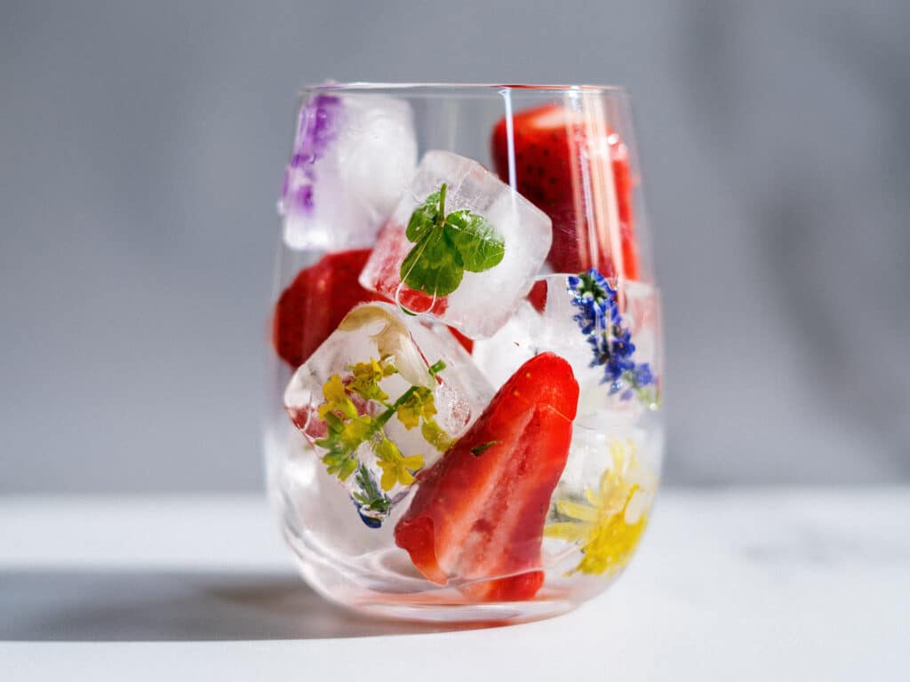 Alameda Post - a glass of ice with edible leaves and flowers frozen in the cubes
