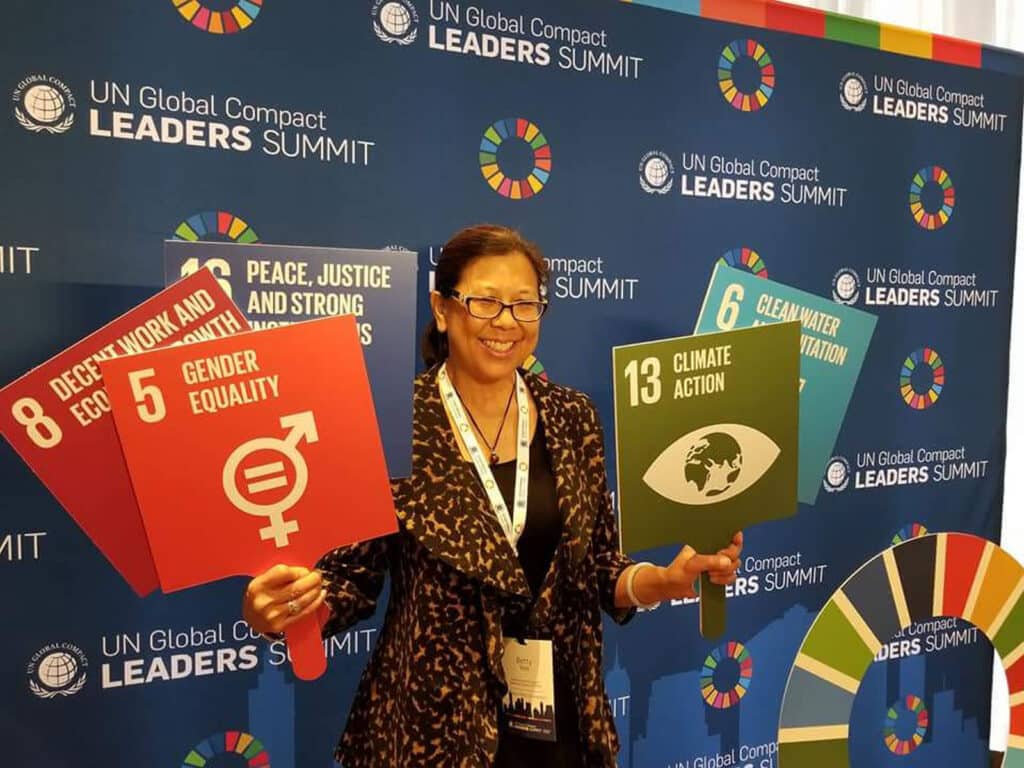 Alameda Post - Betty Yee holds up signs such as "Gender Equality," "Climate Action," and others in front of a backdrop that says UN Global Leaders Summit