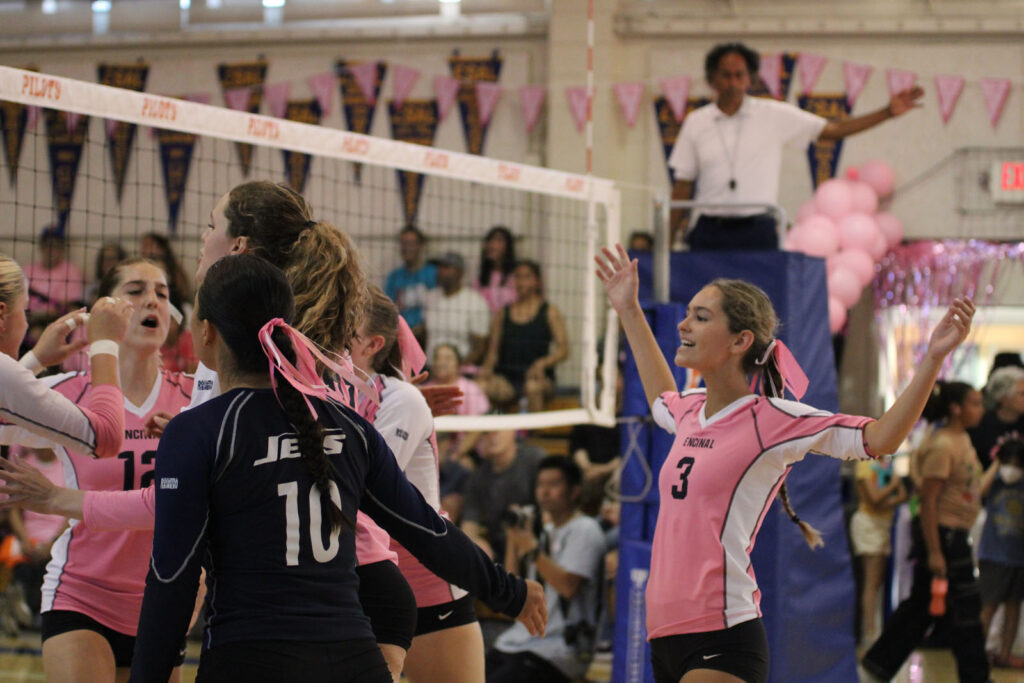 Alameda Post - a volleyball match where players are wearing pink ribbons in their hair. One player celebrates with their hands up