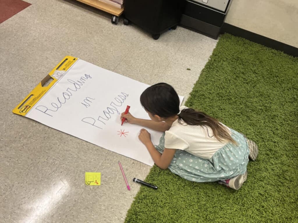 Alameda Post - an elementary schooler writes "Recording in Progress" on a large piece of paper