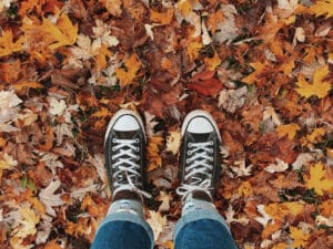 Alameda Post - a photo taken by someone looking down at the ground. The ground is covered in fall colored leaves, and the person is wearing Converse