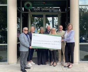 Alameda Post - seven people stand in front of an AMP building holding a large check for Power Up for Learning