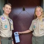 Alameda Post - two Alameda Scouts stand next to a door with doorhangers that announce the food drive