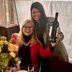 Alameda Post - at a restaurant, Kelly Lux holds up a bottle of wine and smiles while Joann Guitarte poses next to her