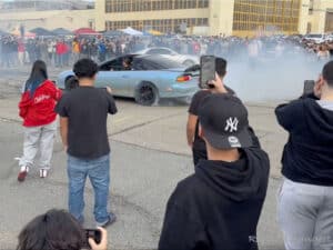 Alameda Post - people cather around a car with their phones out an an Alameda Point sideshow