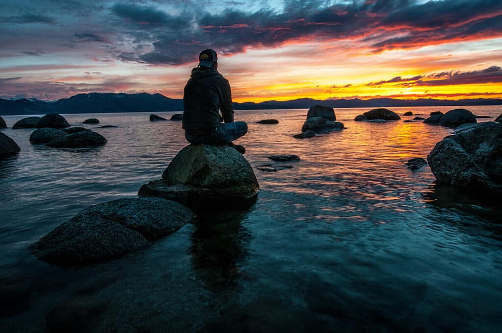 Alameda Post - a person sitting on a rock in the ocean watching the sunset