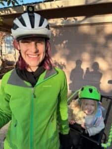 Alameda Post - a smiling cyclist and their child in a seat on the back of the bike