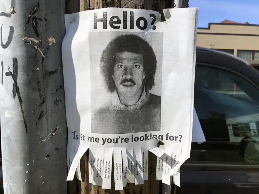 Alameda Post - a flyer on a telephone pole with a photo of Lionel Richie saying "Hello? Is it me you're looking for?"