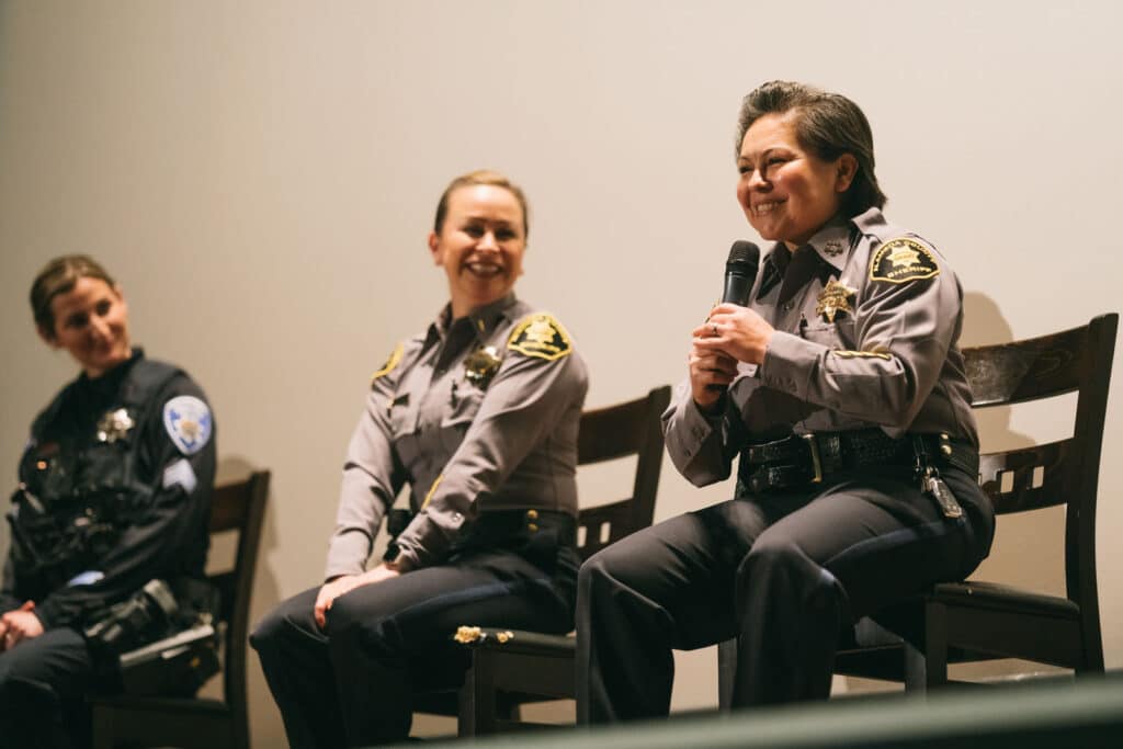 Alameda Post - three female first responders in uniform sit on stage. One smiles and talks into a microphone.
