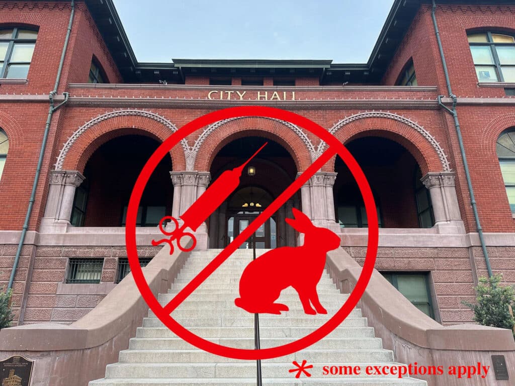 Alameda Post - City Hall with a circle and slash of a bunny and a syringe, indicating no animal testing. IN the bottom right hand corner is an asterix with the words "some exceptions apply"