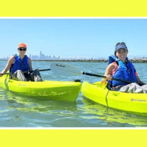 Alameda Post - two women in kayaks float in Ballena Bay with San Francisco in the distance on a Sea Trek tour