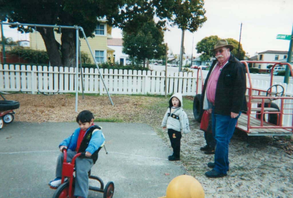 Alameda Post - a child rides a tricycle while another child and an adult look on