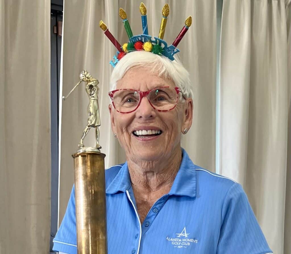 Alameda Post - A golfer on her 90th birthday, wearing a birthday crown, holding a golf trophy. 
