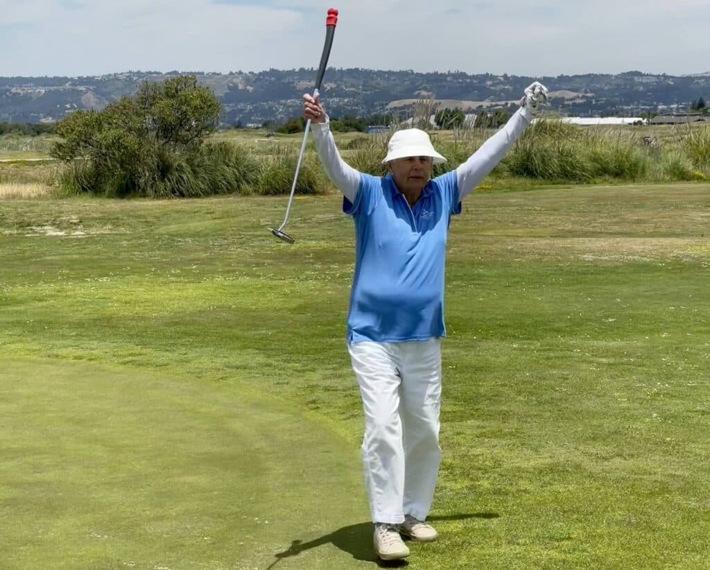 Alameda Post - A golfer raises her hands in victory on the green. 