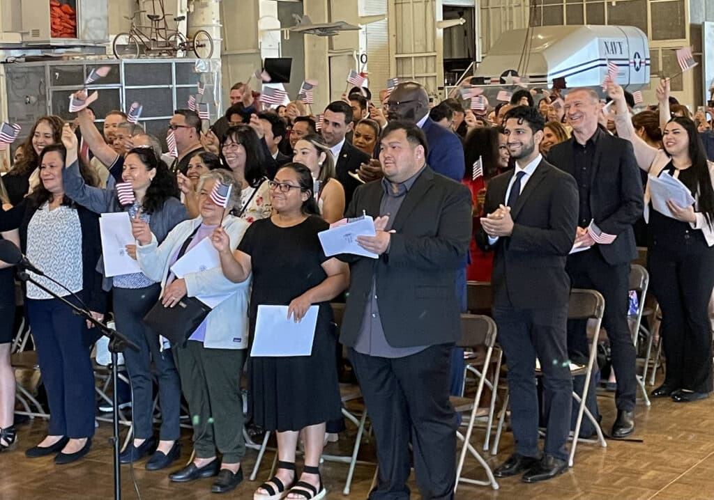 Alameda Post - new citizens aboard the USS Hornet wave small American flags and smile