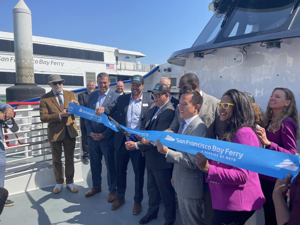 Alameda Post - people gathered on a dock smile and cut a large ribbon