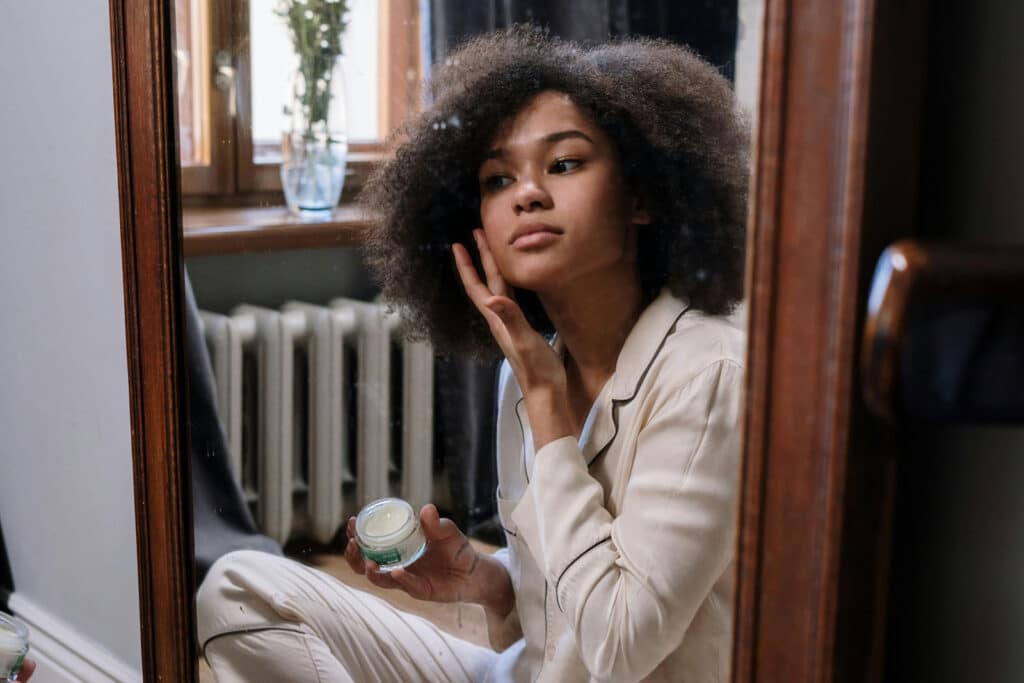 Alameda Post - a woman sits in front of a mirror and rubs a cream into her skin