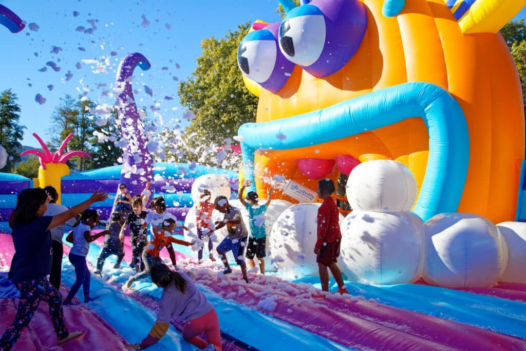 Alameda Post - children play on a huge bounce house as foam sprays around them