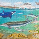 Alameda Post - a photo of the Under the Bay puzzle. Fish, a whale, and a crab swim in the water. Pelicans fly above, and a boat cruises by. The golden gate bridge is in the background.