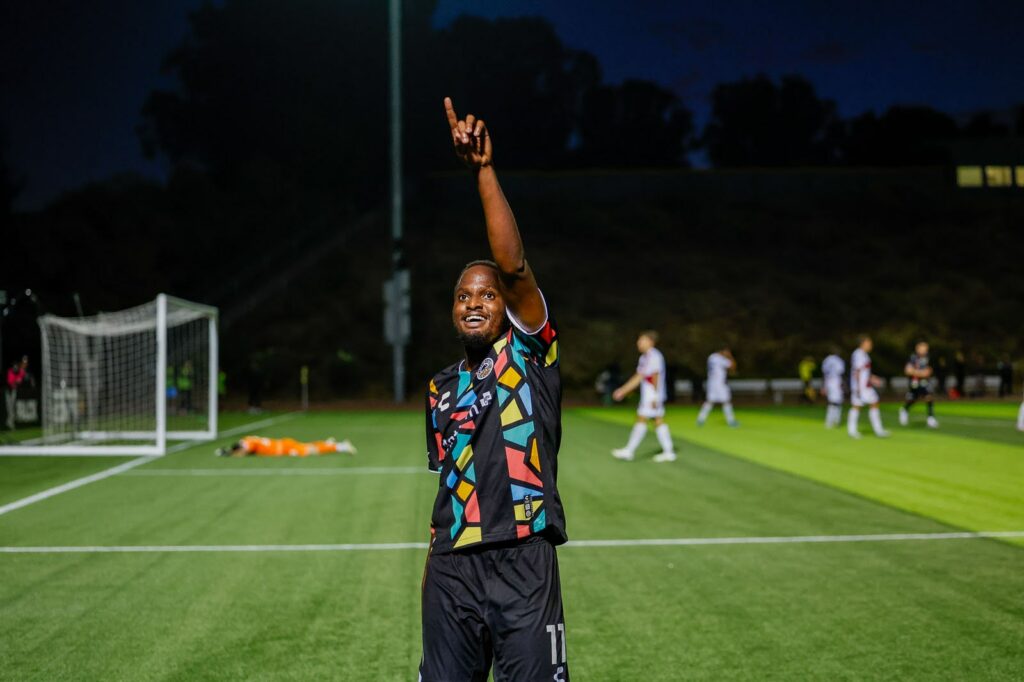 Alameda Post - an Oakland Roots player smiles and holds up the number "1" in a match against Loudoun United