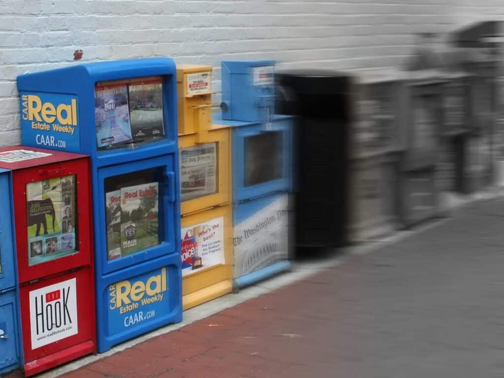 Alameda Post - a photo of newspaper vending machines in a row that get blurrier and less colorful from left to right