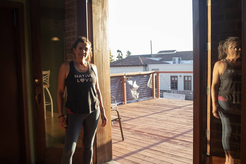 Alameda Post - a woman in workout gear stands next to an open door leading onto a deck
