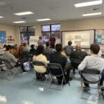 Alameda Post - two people stand at the front of a room and give a powerpoint presentation to a crowd of about 20
