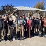 Alameda Post - a group of fourteen people stand with shovels in front of a piece of machinery at the new Alameda Food Bank groundbreaking ceremony