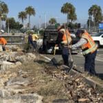 Alameda Post - workers in safety vests work to get plastic trash and debris out from the ground in between the road and Seaplane Lagoon