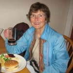 Alameda Post - Pat Gannon sits at a dinner table and smiles at the camera